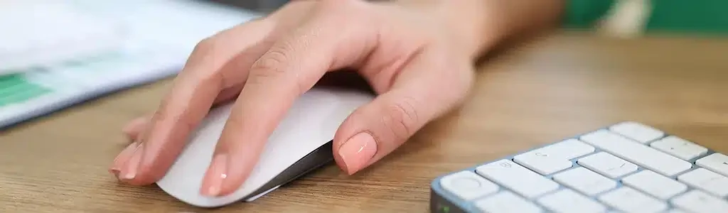 A person using a wireless mouse next to a computer keyboard on a wooden desk, while considering the costs of a website redesign for 2024.