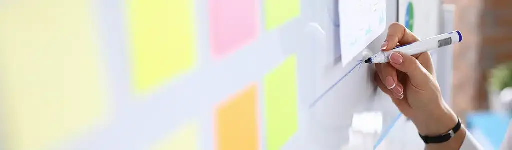 A person writes on a whiteboard with a marker, surrounded by colorful sticky notes detailing the 2024 website redesign.